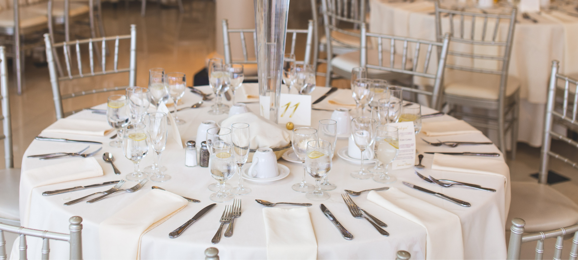 silver chairs around white circular table with silverware and glasses on it