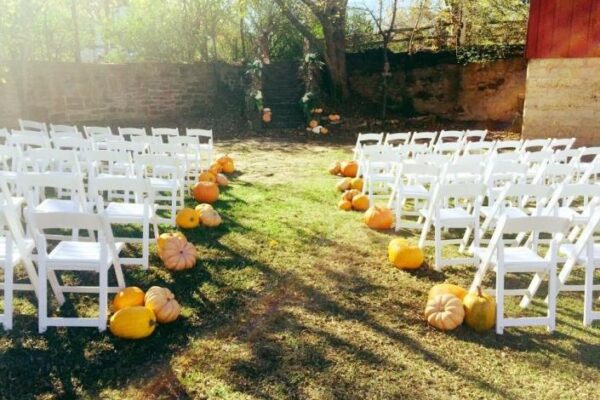 white chairs in backyard wedding with pumpkins at end of row