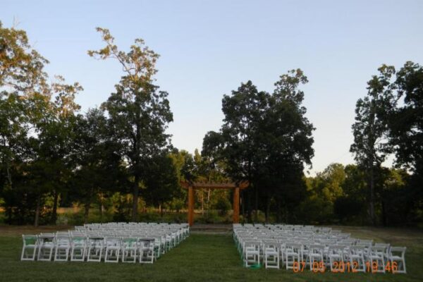 wooden arch for wedding ceremony in front of trees and white chairs.