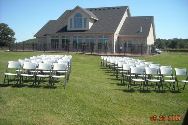 white chairs in grass backyard of tan brick house for wedding ceremony
