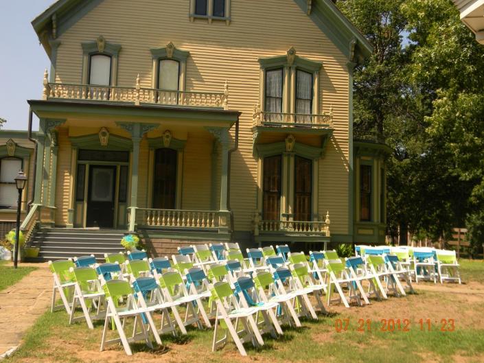 White chairs for wedding ceremony with green/blue ribbons in front yard.